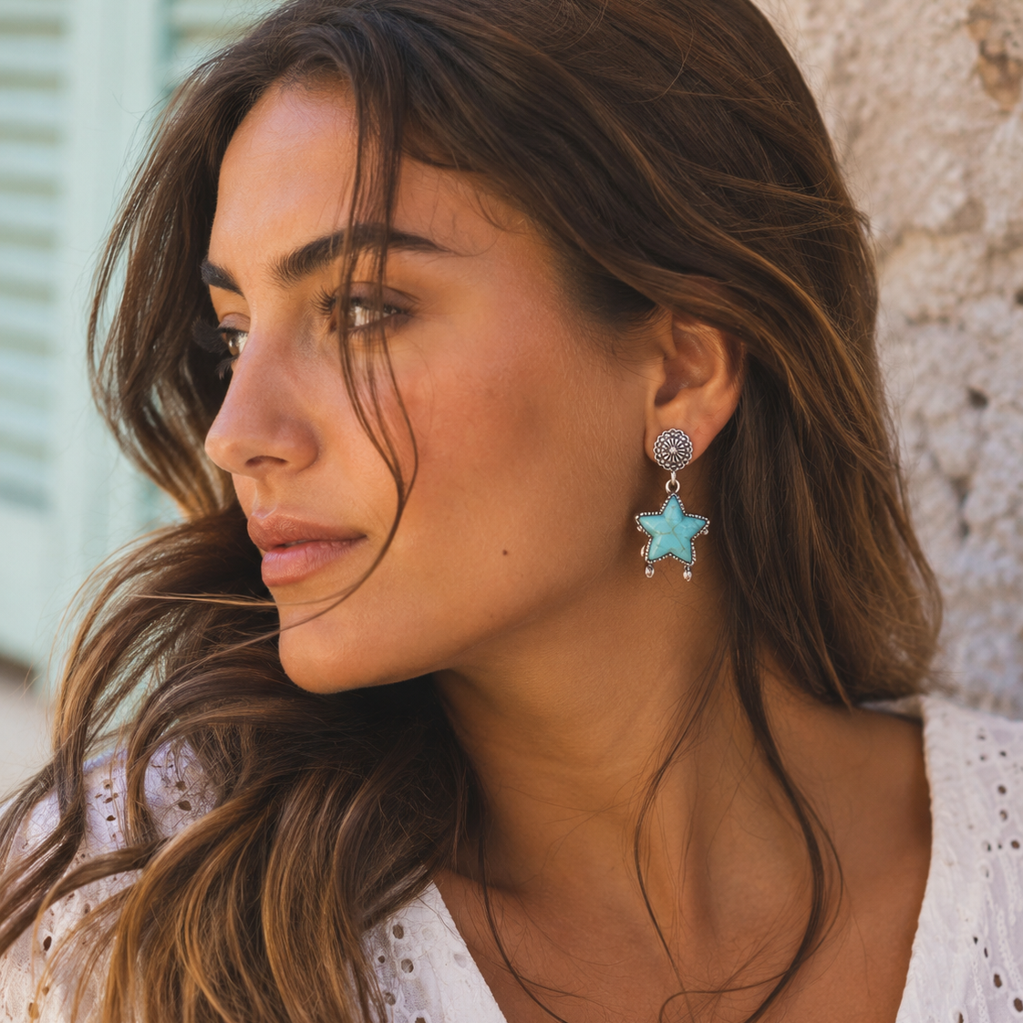 Woman wearing turquoise star-shaped earrings against a stone wall.