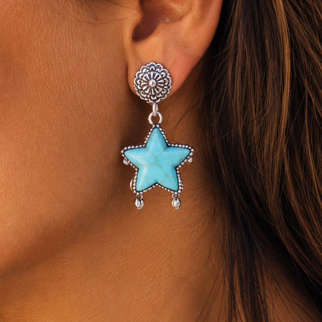 Turquoise star earring worn by a person with brown hair.