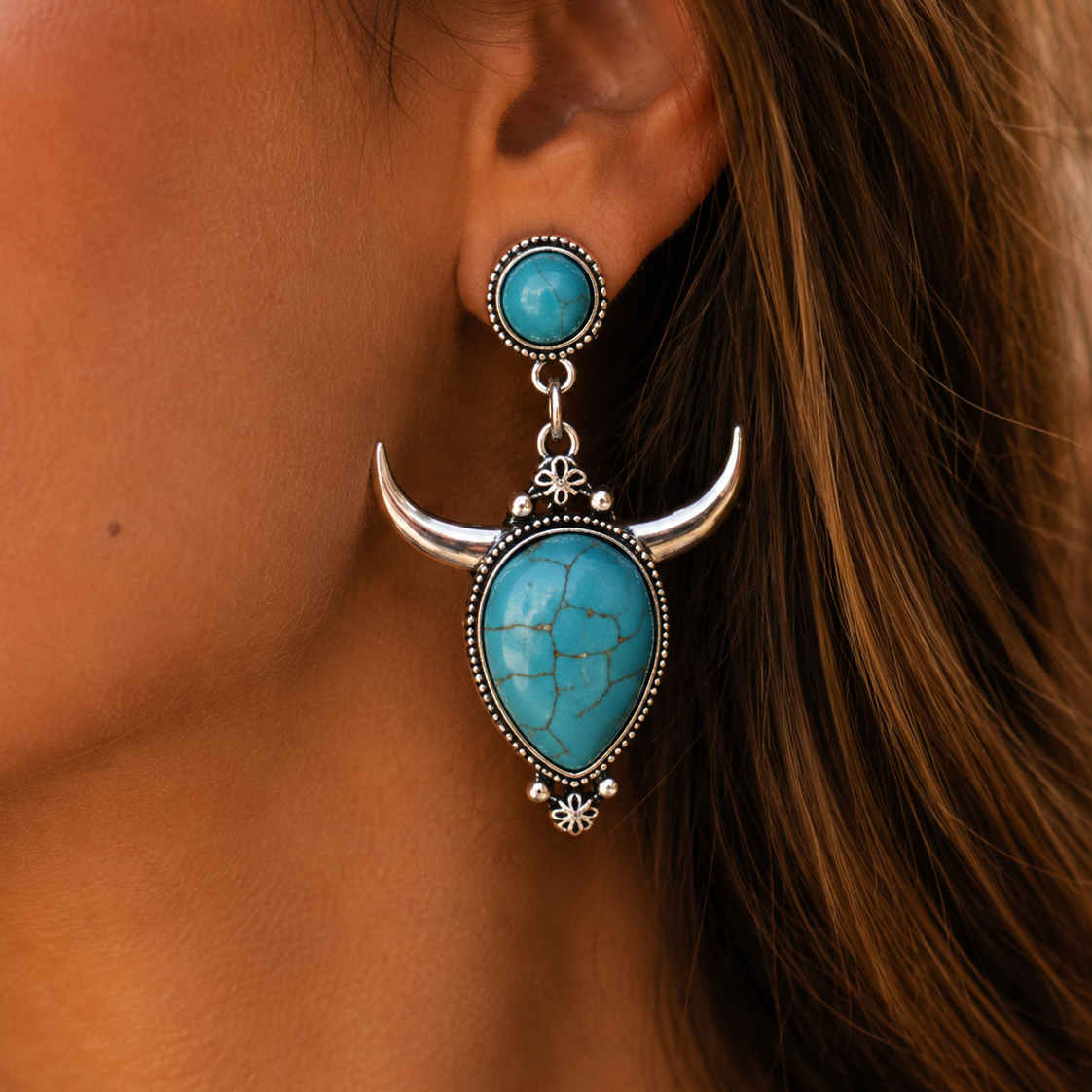Turquoise and silver earrings worn by a person with brown hair.